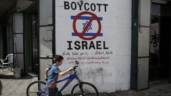 A Palestinian boy walks with his bicycle past past a mural calling people to boycott Israeli goods in the al-Azzeh refugee camp near the West Bank city of Bethlehem on September 17, 2014. There have been growing calls for an economic, academic and cultural boycott of Israel over alleged human rights violations, including in Gaza, where a recent 49-day conflict has killed more than 2,100 Palestinians, most of them civilians. AFP PHOTO/ AHMAD GHARABLI (Photo credit should read AHMAD GHARABLI/AFP/Getty Images)