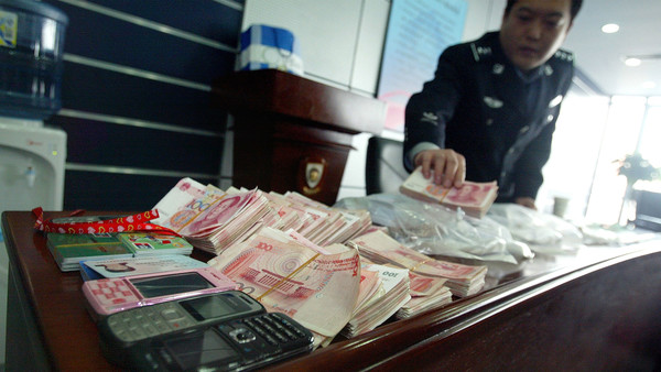 A Chinese policeman shows off cash and other seized items after a crackdown on a Taiwanese money laundering syndicate, during a press conference in Beijing on March 26, 2009. Experts fear the export-dependent Chinese economy slowing to 6.8 percent growth in the final quarter of 2008, and rising unemployment figures could cause a crime wave as China's 1.3 billion people struggle with the consequences of the global meltdown. CHINA OUT GETTY OUT AFP PHOTO