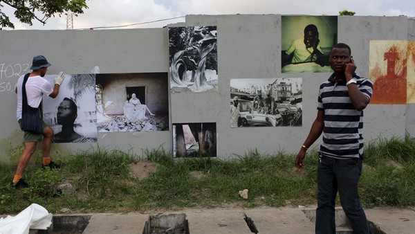 A pedestrian walks by as photographer Robin Maddock pastes a photograph on a wall for LagosPhoto festival in Lagos, Nigeria