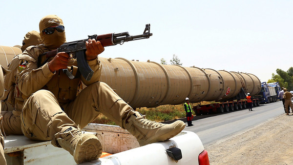 A section of an oil refinery is guarded as it is brought on a lorry to the Kawergosk Refinery, some 20 kilometres east of Arbil, the capital of the autonomous Kurdish region of northern Iraq, on July 14, 2014. The International Energy Agency (IEA) said on July 11, that an offensive by jihadists in northern Iraq had cut output by 260,000 barrels a day in June to 3.17 million, after fighting forced the closure of the country's biggest refinery and slashed production from the giant Kirkuk field. (Photo credit should read SAFIN HAMED/AFP/Getty Images)