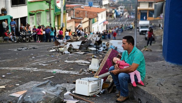Human cost: A father and daughter rest while someone holds their place in a food queue in San Cristobal, Venezuela, amid shortages of basic goods